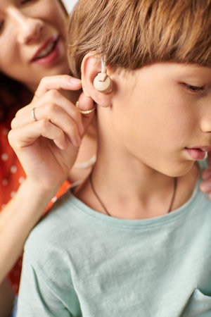 A mother gently helps her hearing impaired son with his hearing device.