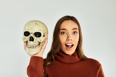 The beautiful young woman playfully holds a skull, showcasing her festive Halloween spirit.の写真素材