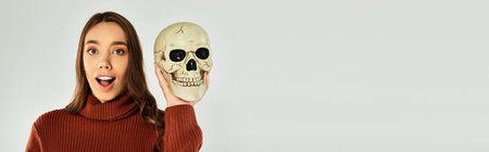 A young beautiful woman joyfully poses with a skull, preparing for Halloween celebrations.の写真素材