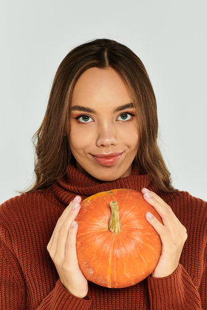 A young, beautiful woman smiles while holding a vibrant pumpkin, embracing the Halloween vibes.の写真素材