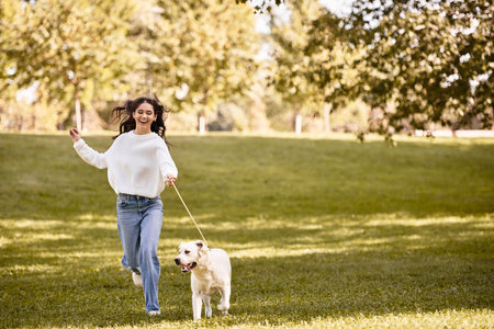 A young woman with long hair runs happily through a park with her playful dog on a sunny autumn day.の写真素材
