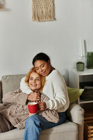 Two women relax together on a couch, sharing laughter and warmth during a cozy afternoon indoors.の写真素材
