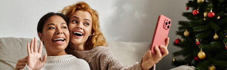 Two women share laughter while taking a playful selfie in their festive living room.