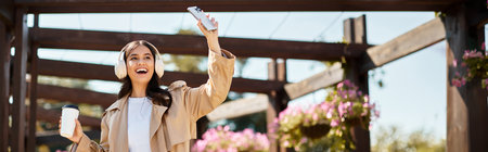 A happy woman in autumn clothes walks in the park, capturing moments on her phone.