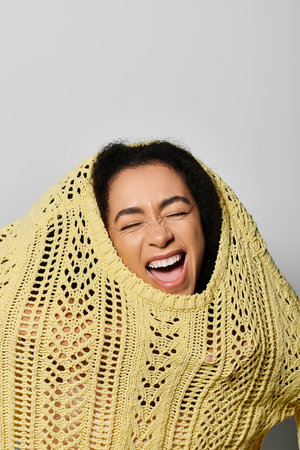 A joyful young woman bursts with laughter while playfully draping a yellow sweater over herself.の写真素材