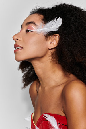 A young woman with curly hair poses gracefully in a vibrant red attire adorned with feathers.の写真素材