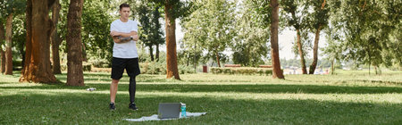 Tattooed young man with prosthetic leg working out in green park, engaging in an online fitness...