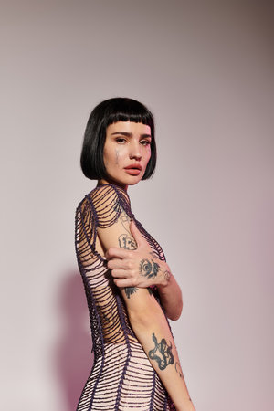 A young woman showcases her tattoos in fashionable clothing, exuding confidence.の写真素材