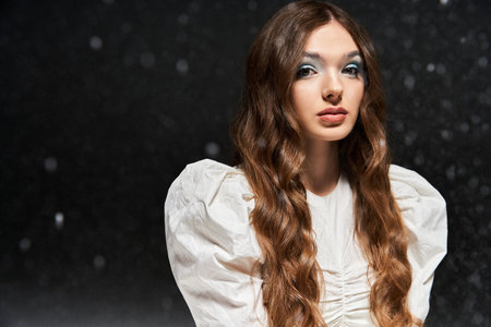 A young woman poses gracefully in a magical setting, highlighting her elegant outfit and wavy hair.