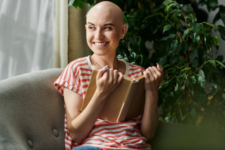 A young, beautiful bald woman smiles brightly while writing in her journal, surrounded by greenery.の写真素材