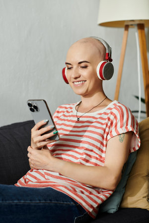 A beautiful bald woman smiles as she listens to music on headphones while using her smartphone.の写真素材