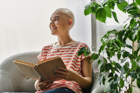 A beautiful young woman with alopecia enjoys reading a book while relaxing in a cozy space.の写真素材