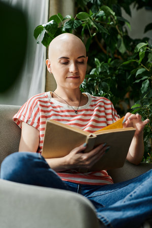 A young woman with alopecia reads intently, surrounded by lush greenery and natural light.の写真素材