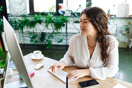 A vibrant young woman engages with her computer at office, immersed in creativity and comfort.の写真素材