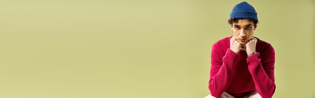 A handsome young man in a pink sweater gazes thoughtfully against a pastel green background.