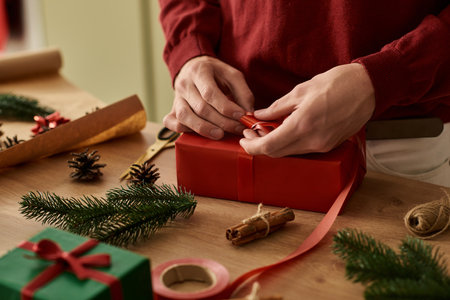 The young man enjoys wrapping a red present, surrounded by festive decorations and supplies.の写真素材