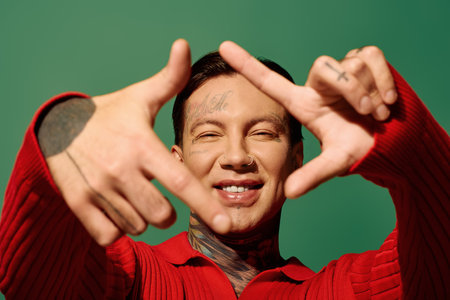 The young man smiles widely, showcasing his tattoos while forming a playful gesture.の写真素材