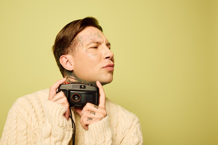 A stylish young man with intricate tattoos contemplates as he poses with a camera.の写真素材