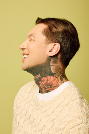 The young man smiles brightly, showcasing his tattoos and casual style in an artistic space.の写真素材