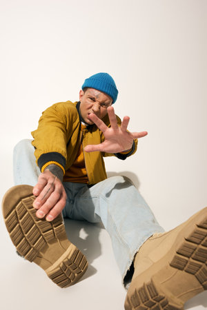 A young man with vibrant tattoos sits back, showcasing his stylish sneakers in a creative pose.