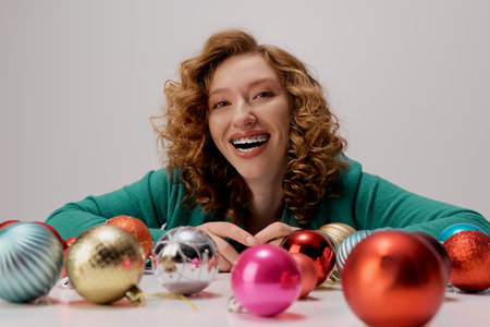 A cheerful young woman posing and colorful ornaments scatter around her.