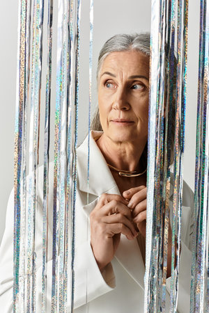 Stylish mature woman with grey hair effortlessly showcases elegance in a white suit on a soft grey...