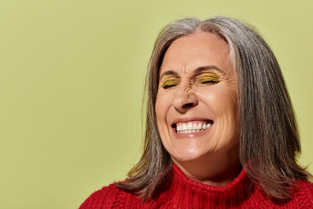 A cheerful mature woman with grey hair beams while wearing a red sweater, perfectly embodying winter...
