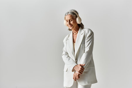A confident and elegant mature woman poses in a sophisticated white suit, showcasing her stunning grey hair.の写真素材