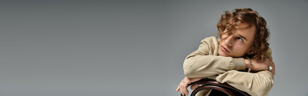 A charming young man dressed in elegant autumn fashion leans against a chair, exuding confidence and style.の写真素材