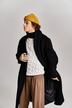 A fashionable young man models confidently in a stylish black coat and bright yellow beanie in a studio.の写真素材