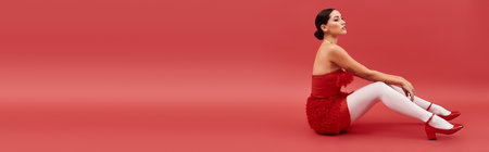 Dressed in a striking red ensemble, a young woman sits gracefully, showcasing artistry and elegance.の写真素材