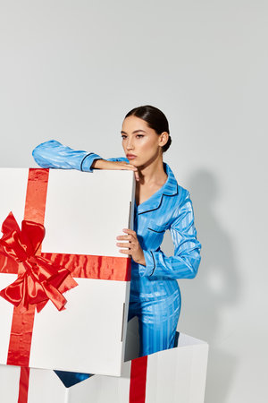 A young beautiful woman elegantly interacts with oversized gift boxes, showcasing her fashion flair.の写真素材