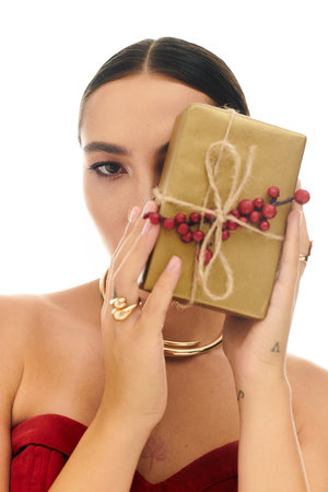 This young woman holds a beautifully wrapped gift close to her face, showcasing holiday spirit.の写真素材