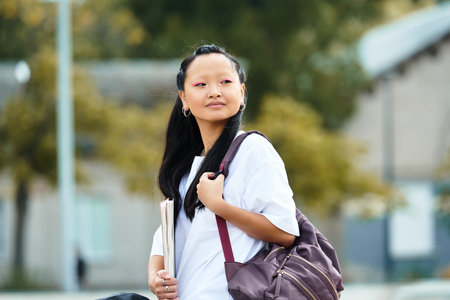 A stylish young Asian student enjoys her time outdoors on campus, embodying youth culture.の写真素材