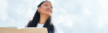 A stylish young Asian student enjoys the outdoors, capturing the essence of youth culture and...