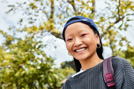 A cheerful young Asian student captures a moment of joy outdoors, showcasing her stylish outfit and uniqueness.の写真素材