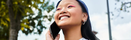 A young Asian student girl embraces youth culture outdoors, engaging in a lively phone conversation.の写真素材