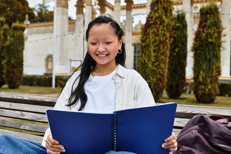 A cheerful young Asian student studies outdoors, enjoying the vibrant atmosphere of the university campus.の写真素材