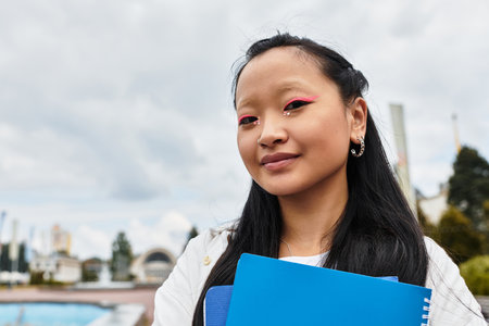A stylish young girl poses confidently with her notebooks, embracing campus culture and diversity.の写真素材