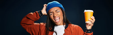 A young woman wearing trendy autumn clothes joyfully holds a warm drink while smiling.の写真素材