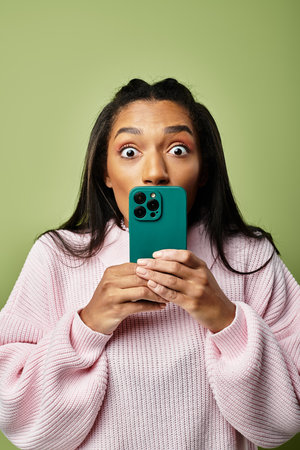 A young woman in warm, stylish clothes shows excitement while using her smartphone.の写真素材