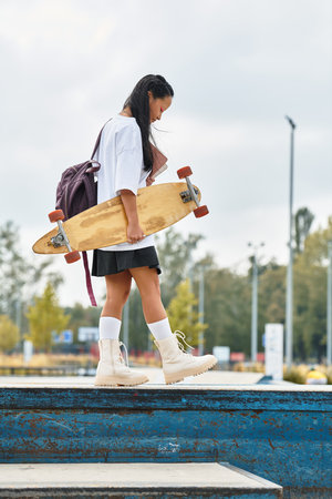 A stylish young Asian girl holds a skateboard while exploring the vibrant outdoor atmosphere of the city.の写真素材