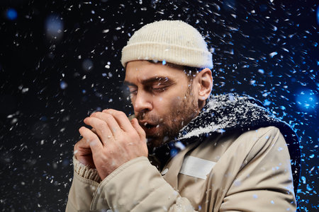 Snowflakes swirl around a young man as he warms his hands against the chilly winter air.