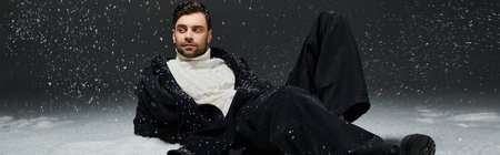 A stylish young man relaxes playfully in the snow, looking handsome in winter attire.の写真素材