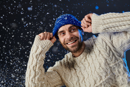 A young man warmly dressed smiles as snowflakes fall around him in a winter wonderland.の写真素材