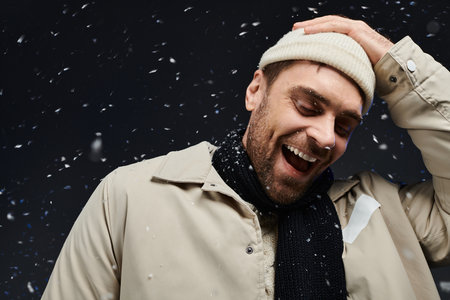 A handsome young man smiles widely while snowflakes fall gently around him during winter.
