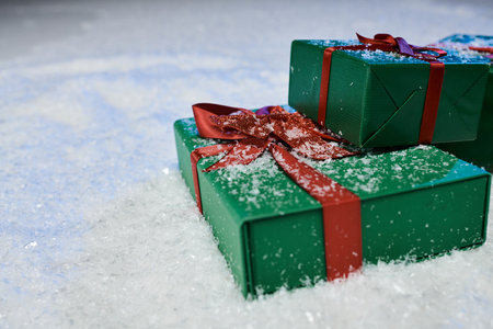 Two beautifully wrapped green gifts with red ribbons sit quietly on a blanket of sparkling snow.