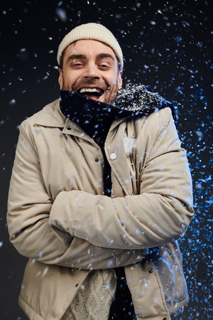 A young man with a joyful smile stands in the snow, embracing the winter season.