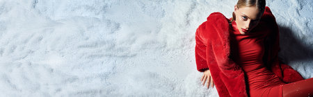 A beautiful woman lounges gracefully on the snow, dressed in red, enjoying the winter atmosphere.の写真素材