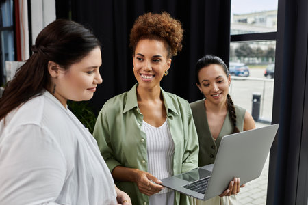Three professional women share ideas while reviewing a laptop in an inviting office environment.の写真素材